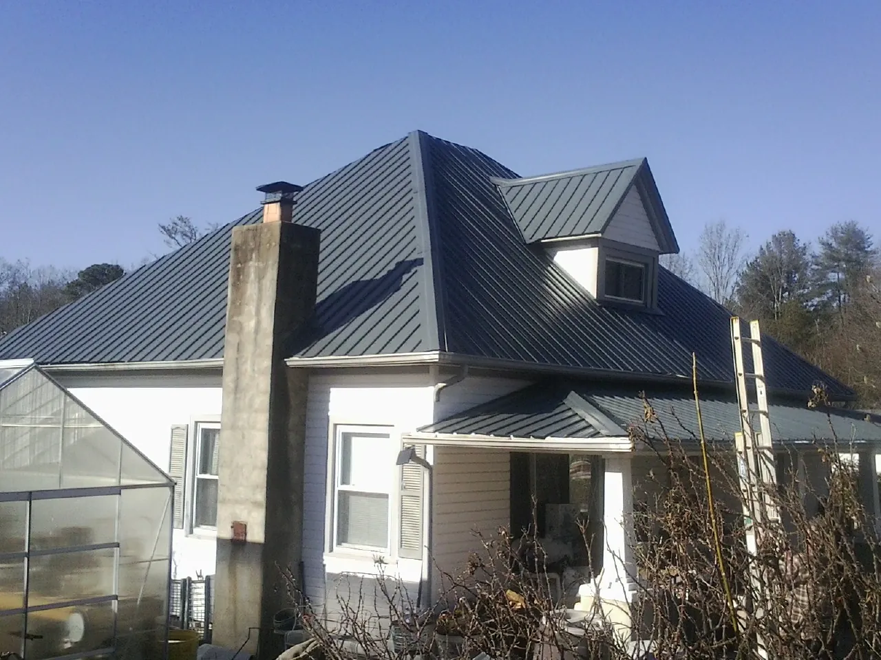 Dark blue standing seam metal roof on a white farmhouse with dormer — Slate & Tile Roof Repair by Roofing Brothers in Benson