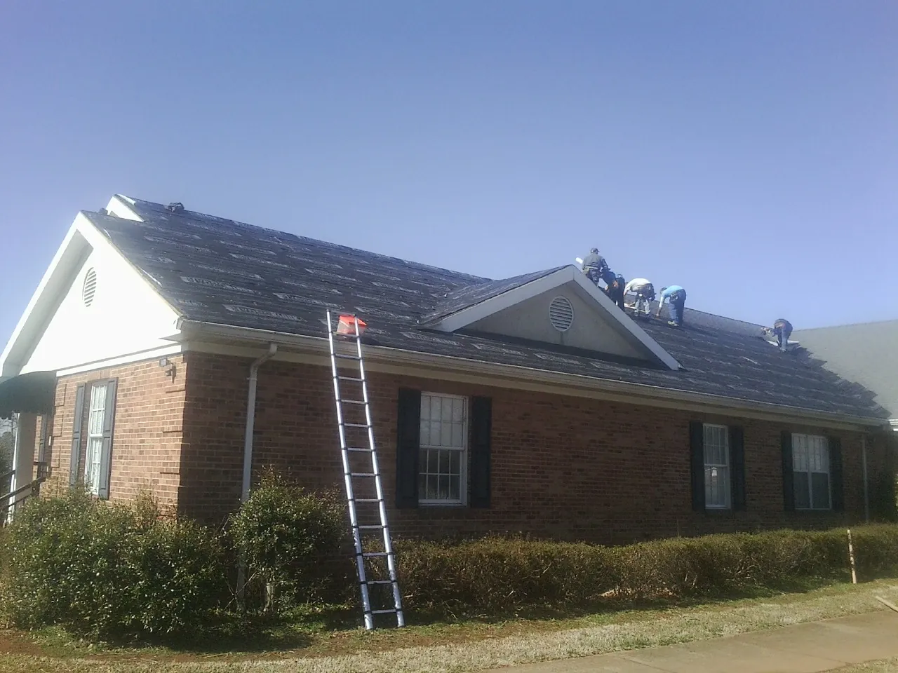 Crew tearing shingles off a brick ranch roof with a ladder set — Metal Roof Repair work by our crew in Benson