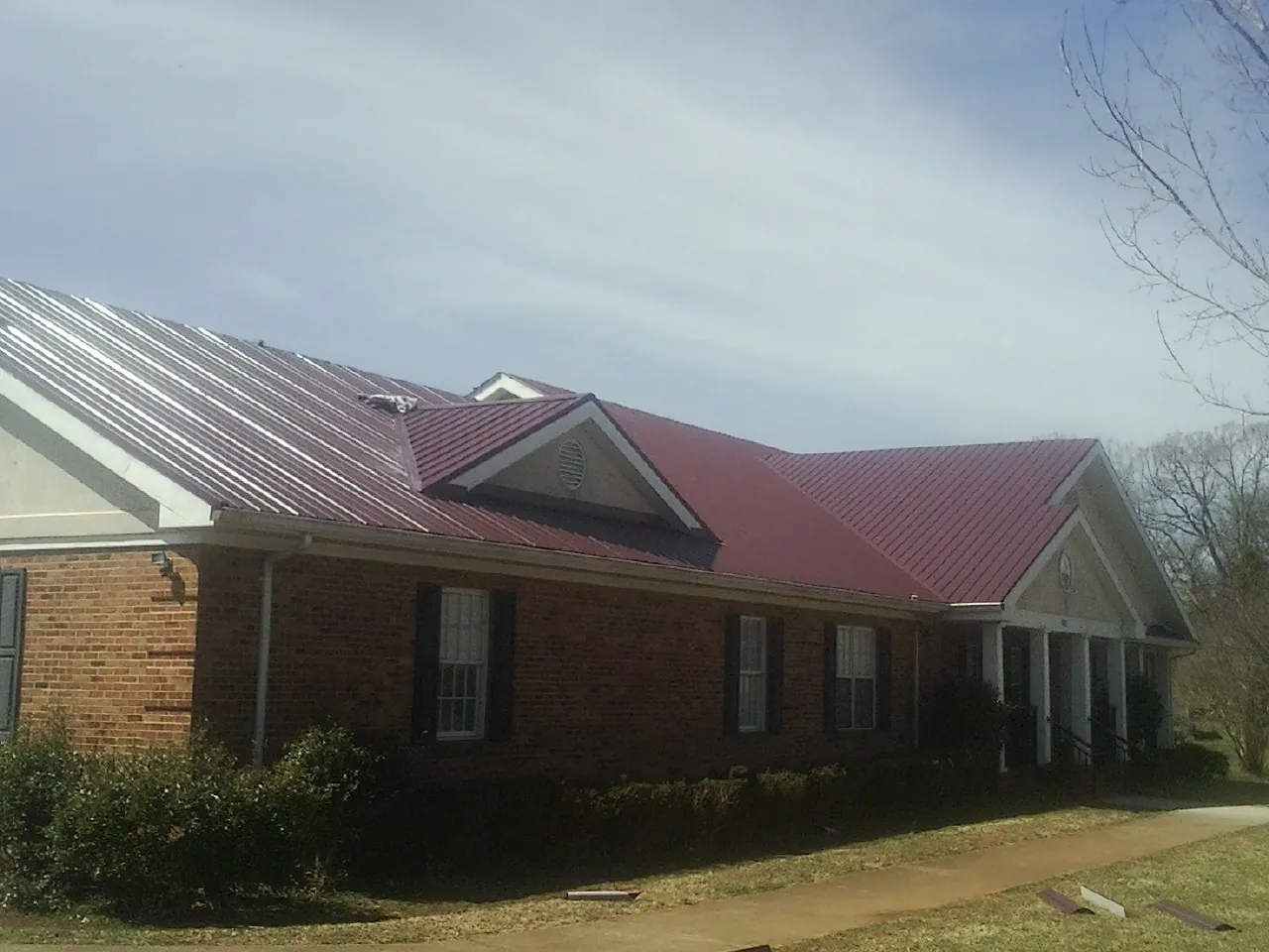 Red metal roof with gabled entries on a long brick building, from a Hail Damage Roof Repair job in Benson