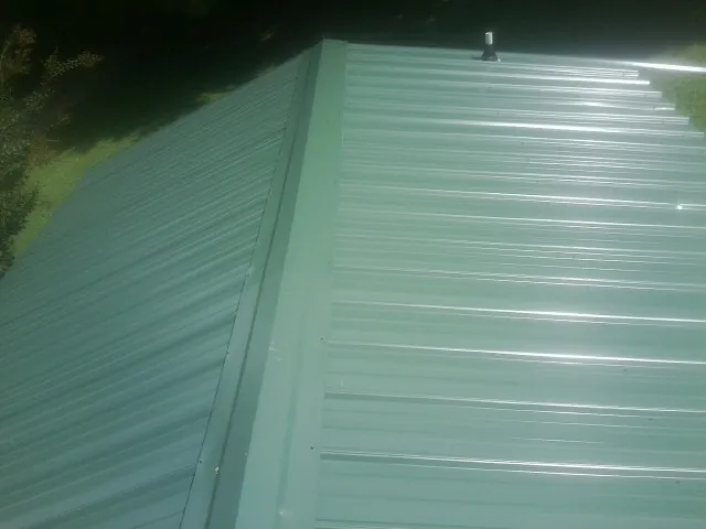 New green metal panels meeting at the ridge of a roof — Flat Roof Repair work by our crew in Benson